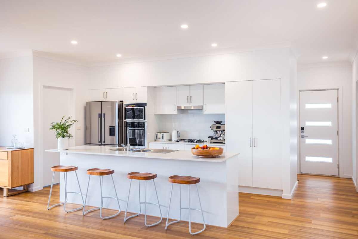 Fresh Modern Kitchen with large pantry and warm timber floors and an Island Bench opening into the living area